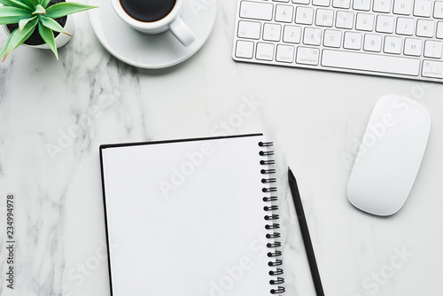 Business composition with white computer keyboard, mouse, coffee cup, artificial plant and notebook with pencil on white marble background. Coffee break at the office concept. Top view with copy space