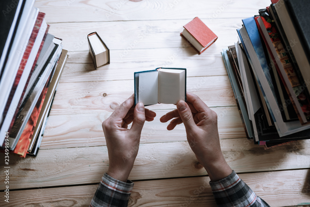 Fototapeta premium A man reading a miniature book among the big books in the library