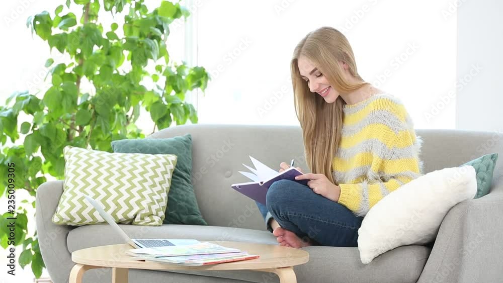 Young woman writing down something in notebook while sitting on sofa and looking at laptop in living room
Young woman writing down something in notebook while sitting on sofa and looking at laptop in living room
