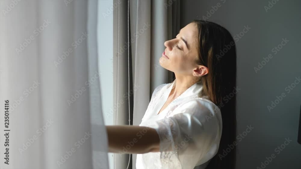 Young woman opening curtains at home on sunny morning
Young woman opening curtains at home on sunny morning