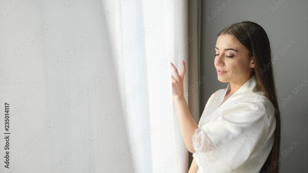 Young woman opening curtains at home on sunny morning
Young woman opening curtains at home on sunny morning