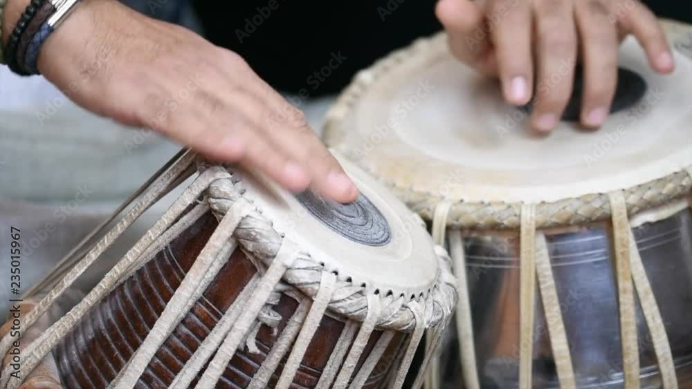 Video of a man's hands (wearing beads) playing the Tabla - Indian classical music percussion instrument - black background.