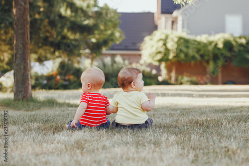 Two adorable little Caucasian babies sitting together in field meadow outside looking different ways. View from back behind. Cchildren in summer park. Talking communication with friend concept photo