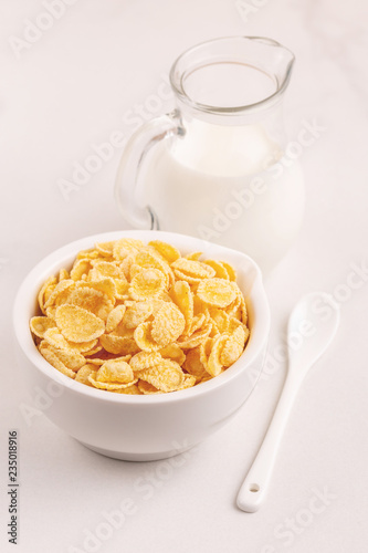 Crispy corn flakes in bowl with jar of milk