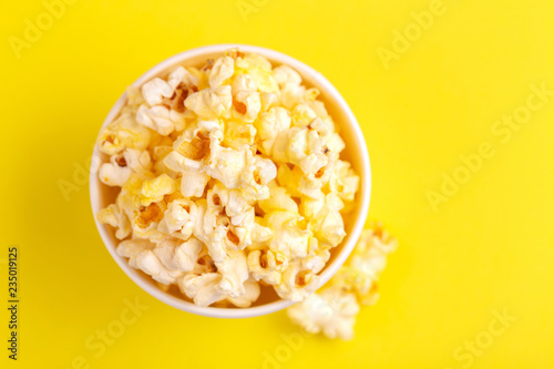Tasty salty popcorn in paper cup on bright yellow backgraund
