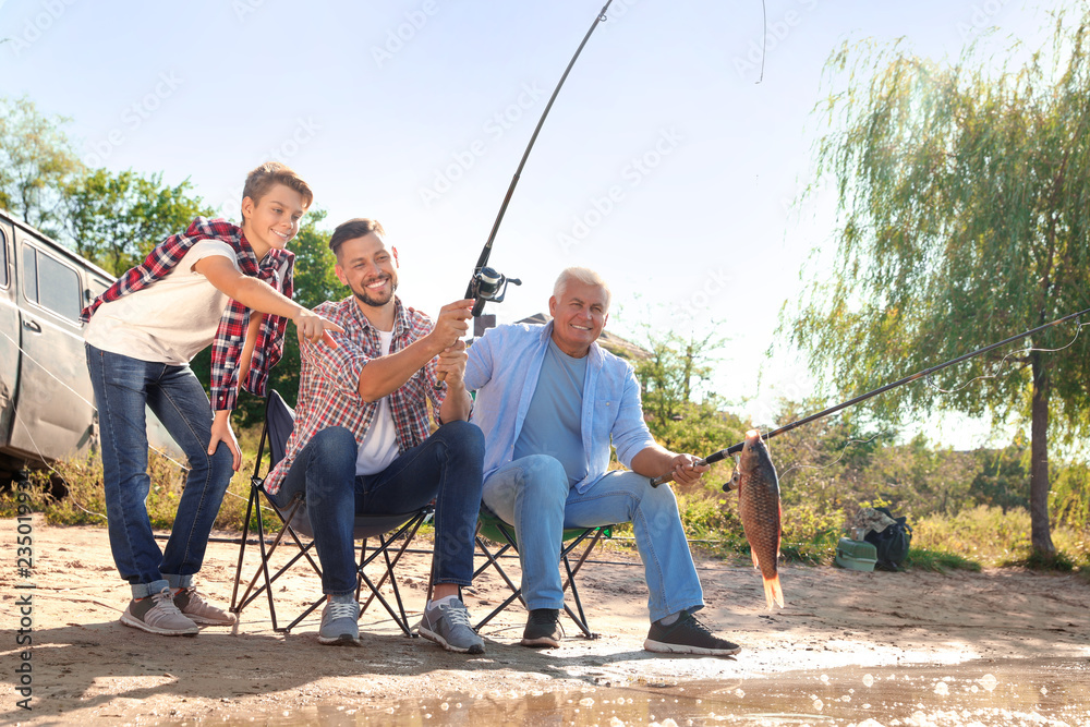 Naklejka premium Happy family fishing together from riverside on sunny day