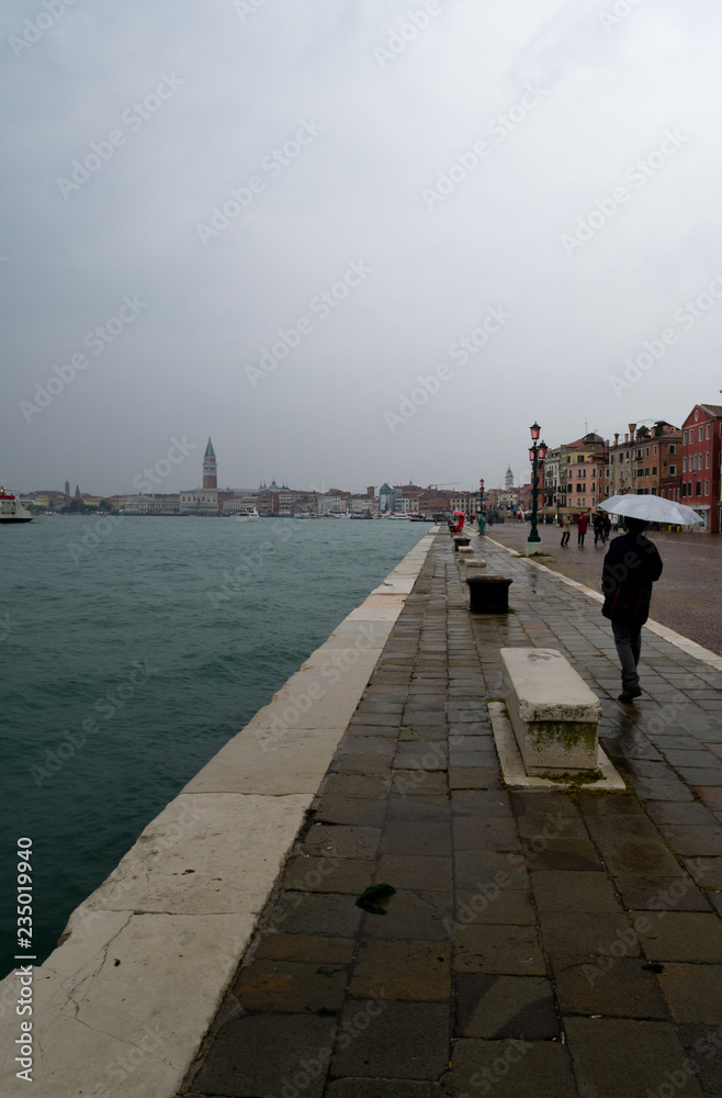 Rainy day in Venice. The sidewalk next to the sea is wet and reflect the low light of the sky.