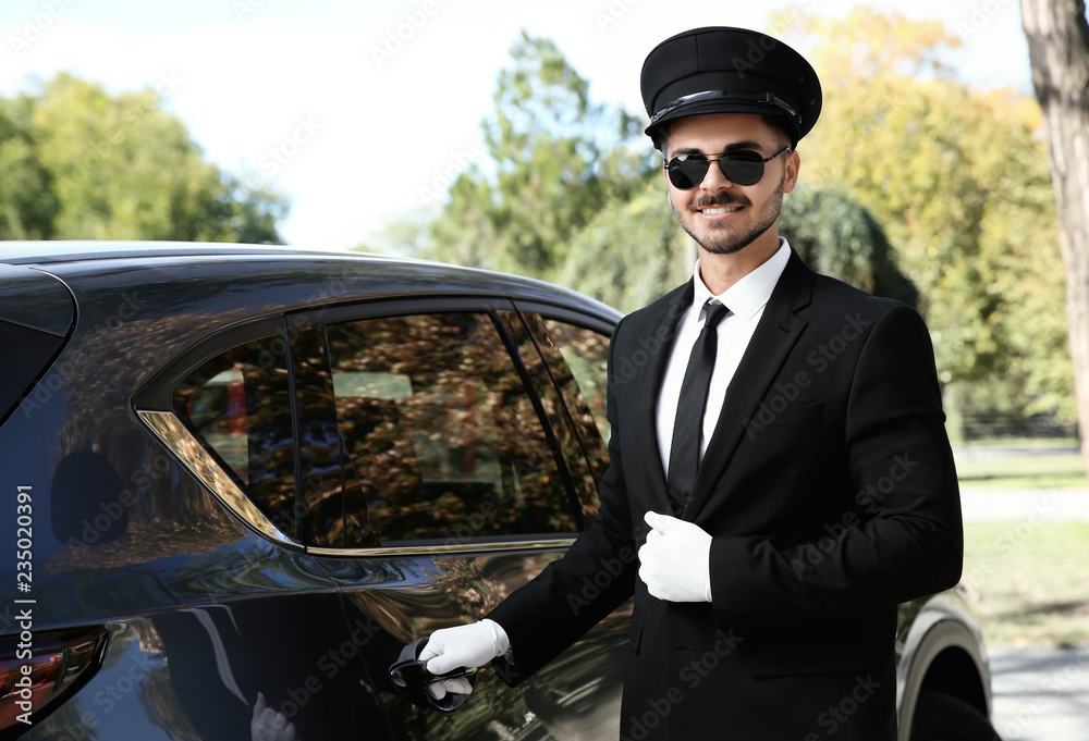 Naklejka premium Young handsome driver opening luxury car door. Chauffeur service