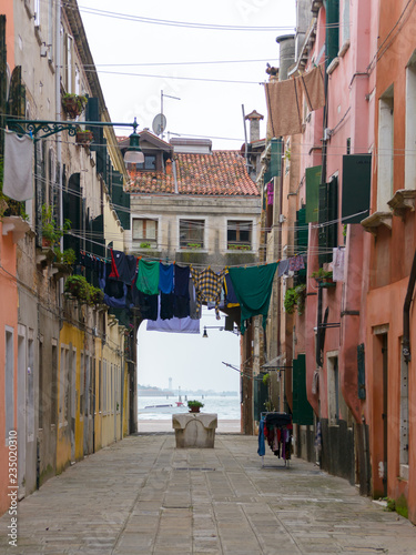 Fototapeta Naklejka Na Ścianę i Meble -  A not touristy spot in Venice, italy. The beauty of this city is also in the hidden spots where architecture is simple. Here a old street with the typical water well and a view to the sea in the back