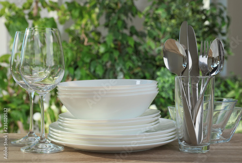 Clean dishes  shiny cutlery and glasses on wooden table against blurred background