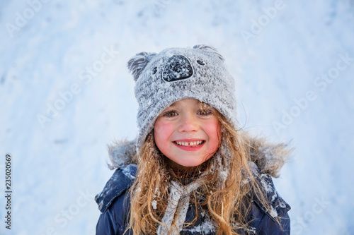 Cute little girl wearing navy jacket and knitted hat playing with snow in winter park. Child walking in snowy forest. Family vacation with kid in mountains