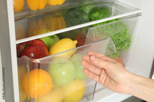 Fototapeta Naklejka Na Ścianę i Meble -  Woman opening refrigerator drawer with fresh fruits, closeup