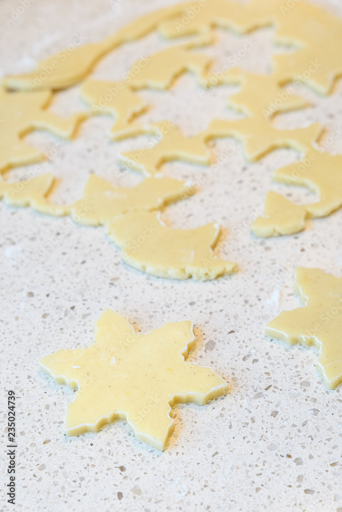 Raw sugar cookie dough rolled out on a light colored granite countertop, with snowflake cookies cut out