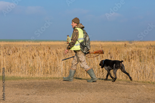 Hunter with a gun and a dog go on the first snow in the steppe, Hunting pheasant in a reflective vest © Mountains Hunter