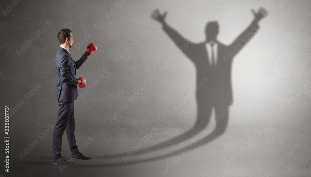 Fototapeta premium Businessman with boxing gloves fighting with disarmed businessman shadow 
