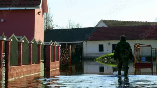Old man walks through the water to the house in flooded area