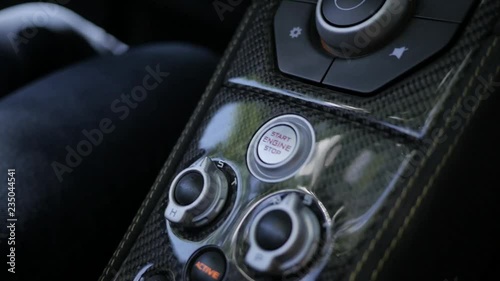 a hand move on start button to start the engine of a sport car with nice carbon fiber cover