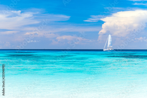 A white sailboat parked at the beach, turquoise waters and beautiful white sand.