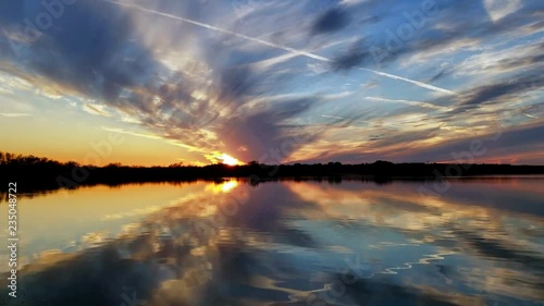 Contrails in Texas time lapse sunset over lake with clouds and blue skies.  Ducks on the water and gulls in the skies.  Small fish feeding.