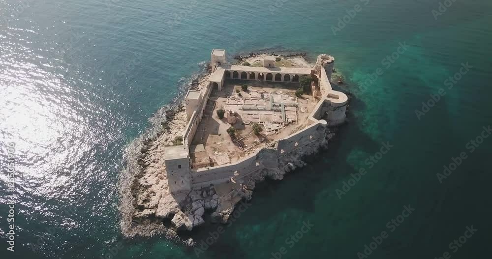 High angle drone aerial view point of interest clockwise rotating above the sunny shimmering turquoise sea water surrounding Kizkalesi Castle island at daytime in Turkey. 4K at 23.97fps