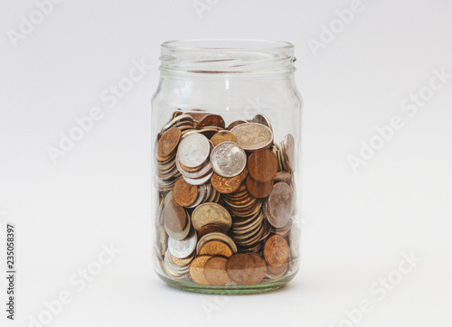 A pile of coins in a glass jar on white background. Piggy bank with money.