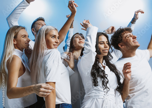 Group of cheerful joyful young people standing and celebrating together over blue studio background