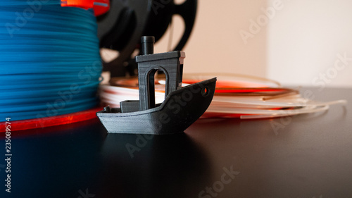 One black 3D printed boat with 3D printer filament on a black background.