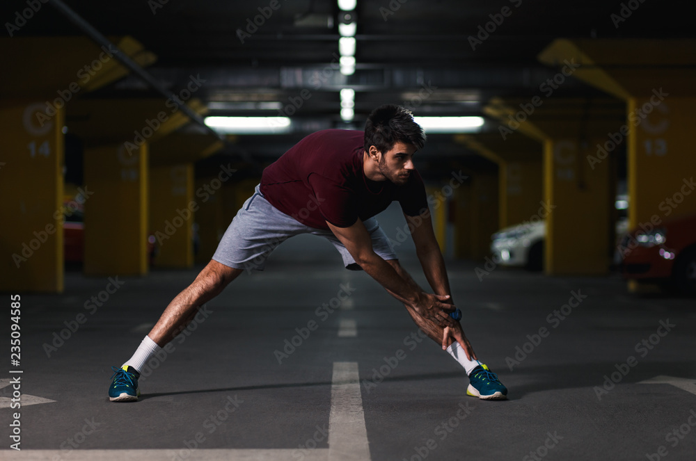 Young male runner stretching his muscles before workout in the underground car parking.