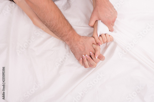 Hands of couple who having sex in bed on white crumpled sheet, focus on hands