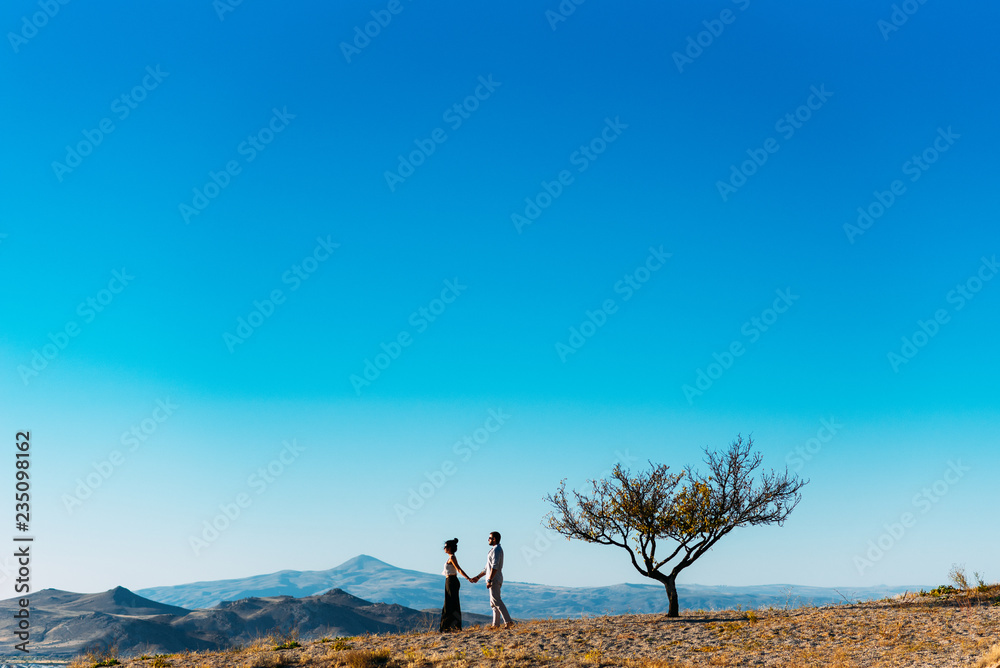 Loving couple meets sunset in the mountains. Couple travels. Lovers in nature. Man and woman watching the sunset. Lovers at sunset. Travel in the mountains. Boy and girl holding hands. Married couple