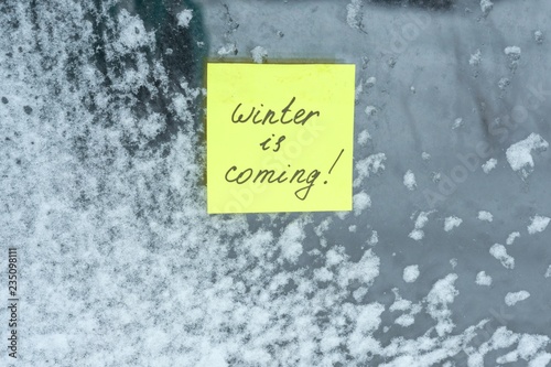 Winter is coming, texture background snow-covered window with a sticker.
