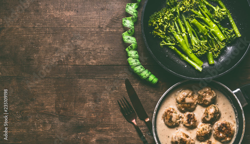 Obraz na plátně Low carb dieting meal with meat balls, blanched broccoli in cooking pan, cutlery and measure tape on wooden table background, top view with copy space