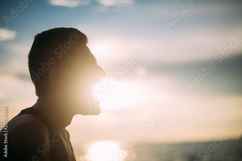 A young man looks at the sunset by the sea. The guy holds the sun in his mouth. Portrait of a young man at sunset by the sea