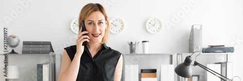 A young girl standing in the office and talking on the phone. photo