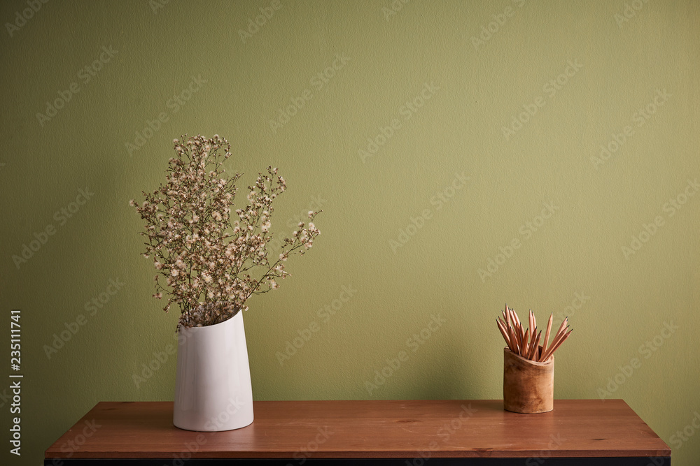 Green wall background, wooden desk and white vase of flower. Wooden pencil.