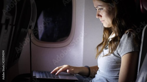 Woman work on notebook in airliner, dark plane salon during nigh flight
