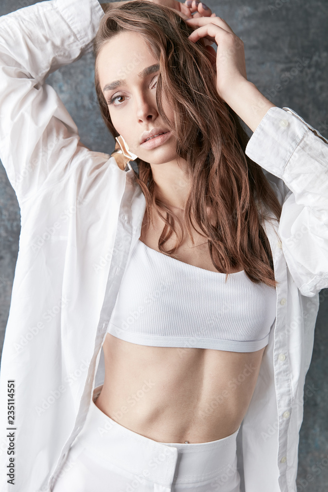 Sexy brunette female model posing in white shirt, top and pants. Studio shot, grey background Sexy brunette female model posing in white shirt, top and pants. Studio shot, grey background