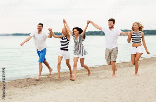 friendship, summer holidays and people concept - group of happy friends in striped clothes running along beach
