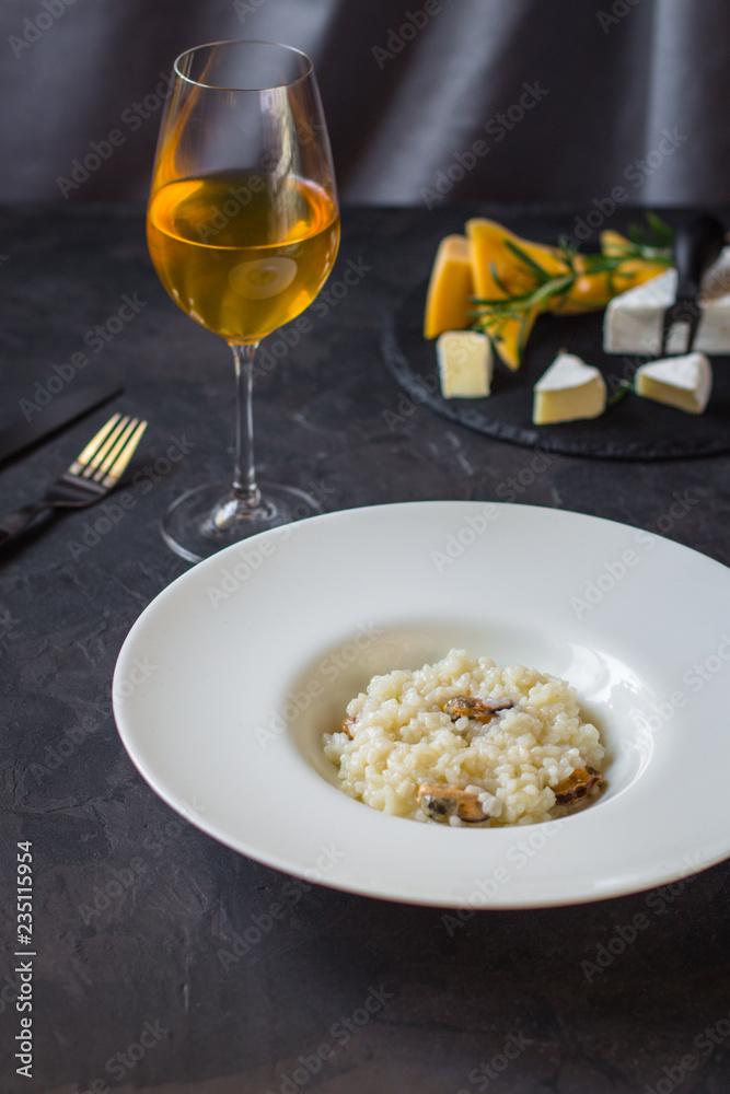 risotto with mussels (seafood rice) in a white plate and a glass of white wine on a dark background