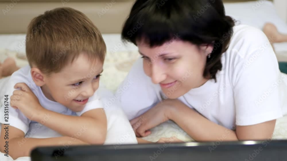 Happy family: mother and child are lying on the bed and happily looking at the laptop screen. Happy family: mother and child are lying on the bed and happily looking at the laptop screen.