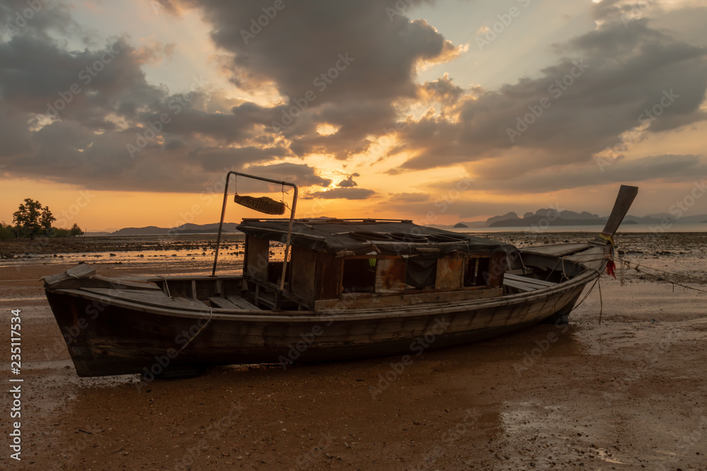 An old wooden boat on a tropical beaching during a beautiful, colorful sunset