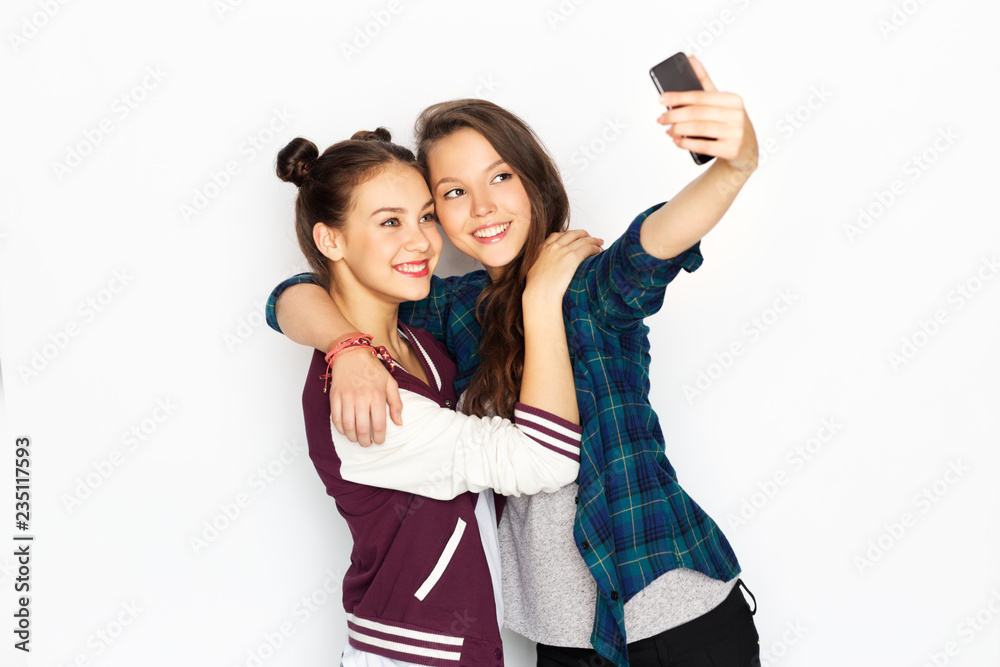 Naklejka premium technology and friendship concept - happy smiling pretty teenage girls taking selfie by smartphone over white background