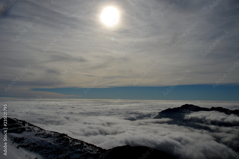 Trekking on the snow-covered mountain ends above a cloud-covered sky