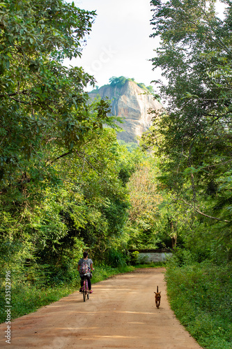 A girl is on her bicycle on the road to the Lion Rock in Sigiriya, Sri Lanka.