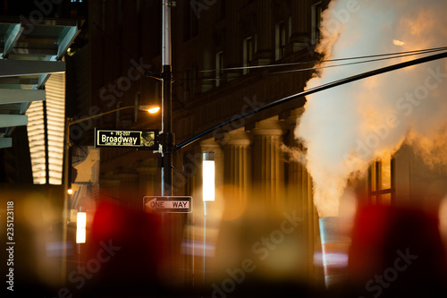 (selective focus) Broadway sign illuminated at night in Manhattan, New York. Steam coming out of the manhole on the right side.