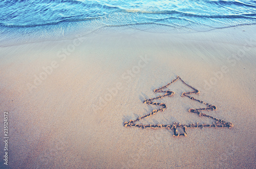 Fototapeta Naklejka Na Ścianę i Meble -  Fir tree drawing on the sand near the sea . Christmas background.