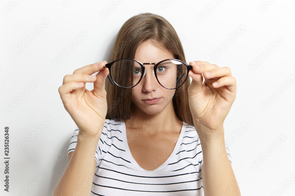 Beautiful cute shortsighted teeage girl in stylish striped t-shirt putting on her first eyeglasses. Vision correction, optics, nearsightedness and myopia concept. Selective focus on spectacles Beautiful cute shortsighted teeage girl in stylish striped t-shirt putting on her first eyeglasses. Vision correction, optics, nearsightedness and myopia concept. Selective focus on spectacles