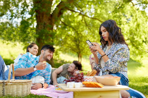 leisure  technology and people concept - woman using smartphone at picnic with friends in summer park
