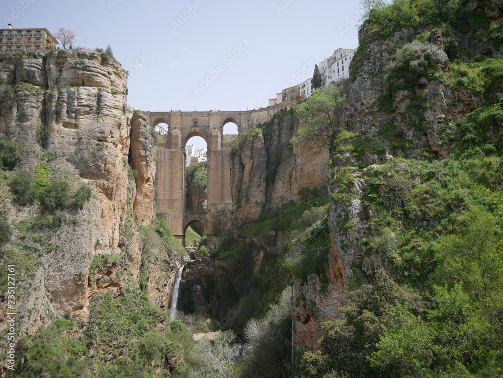 Old bridge connecting two parts of a city on mountains over a canyon with a waterfall in Ronda, Spain