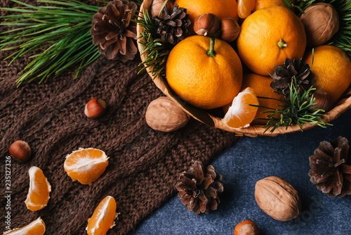 Hazelnuts, walnuts and tangerines decorated with Christmas branches and pine cones on the table in a wooden basket